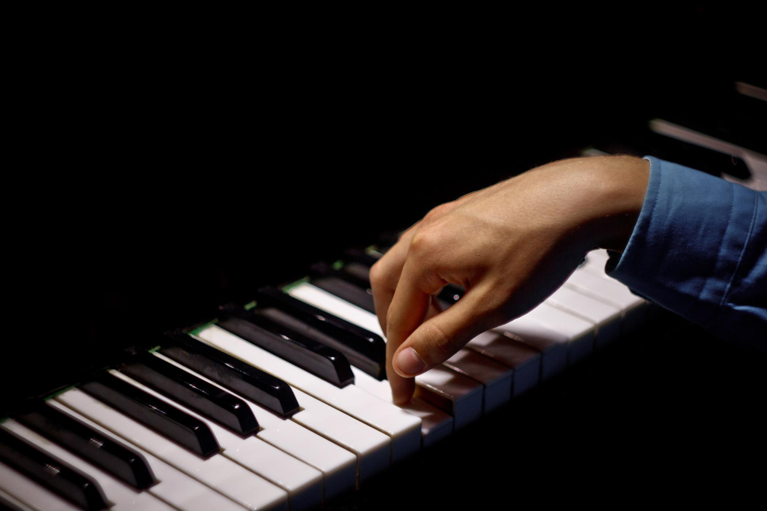 Loş ışıkta akustik piyanonun tuşlarına basan bir yetişkinin eli; Piyano Akademi’nin birebir piyano derslerinde uygulamalı eğitimi vurgulayan detay çekimi.