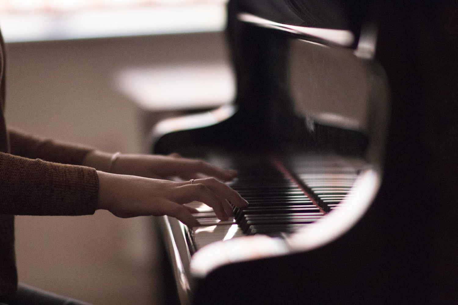 Loş ortamda akustik piyanoda iki eliyle çalan bir öğrencinin siluet şeklindeki yakın plan görüntüsü; Piyano Akademi’de uygulamalı piyano eğitimini gösteren sahne.